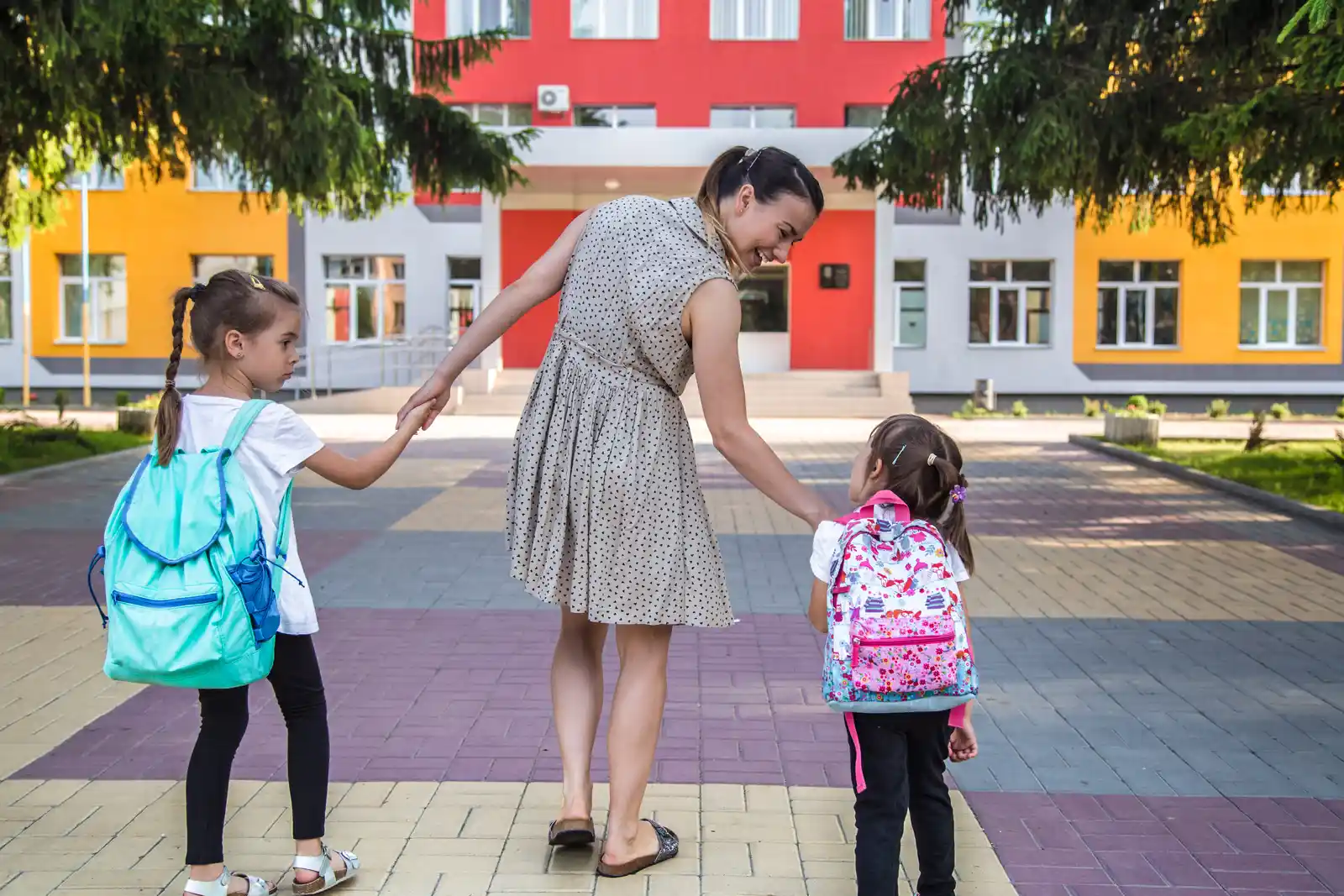 Elementary students with backpacks walking into school with a parent